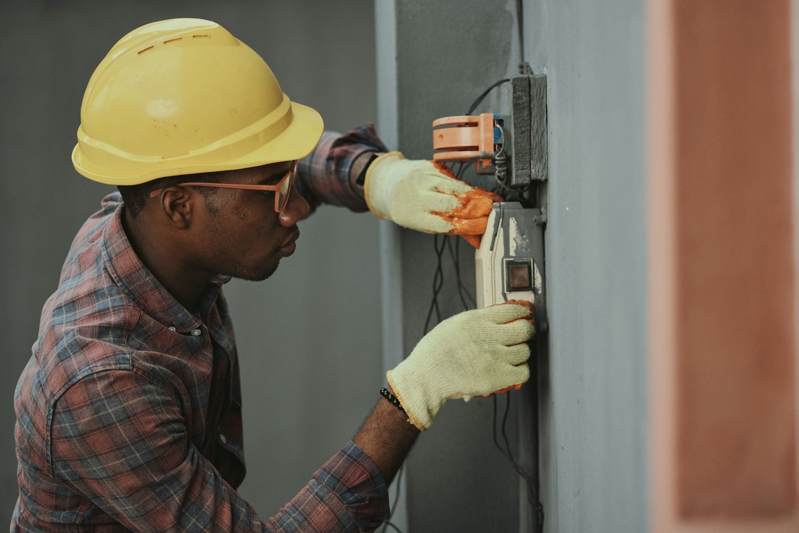 A worker in a hard hat fitting an electrical fixture to a wall.