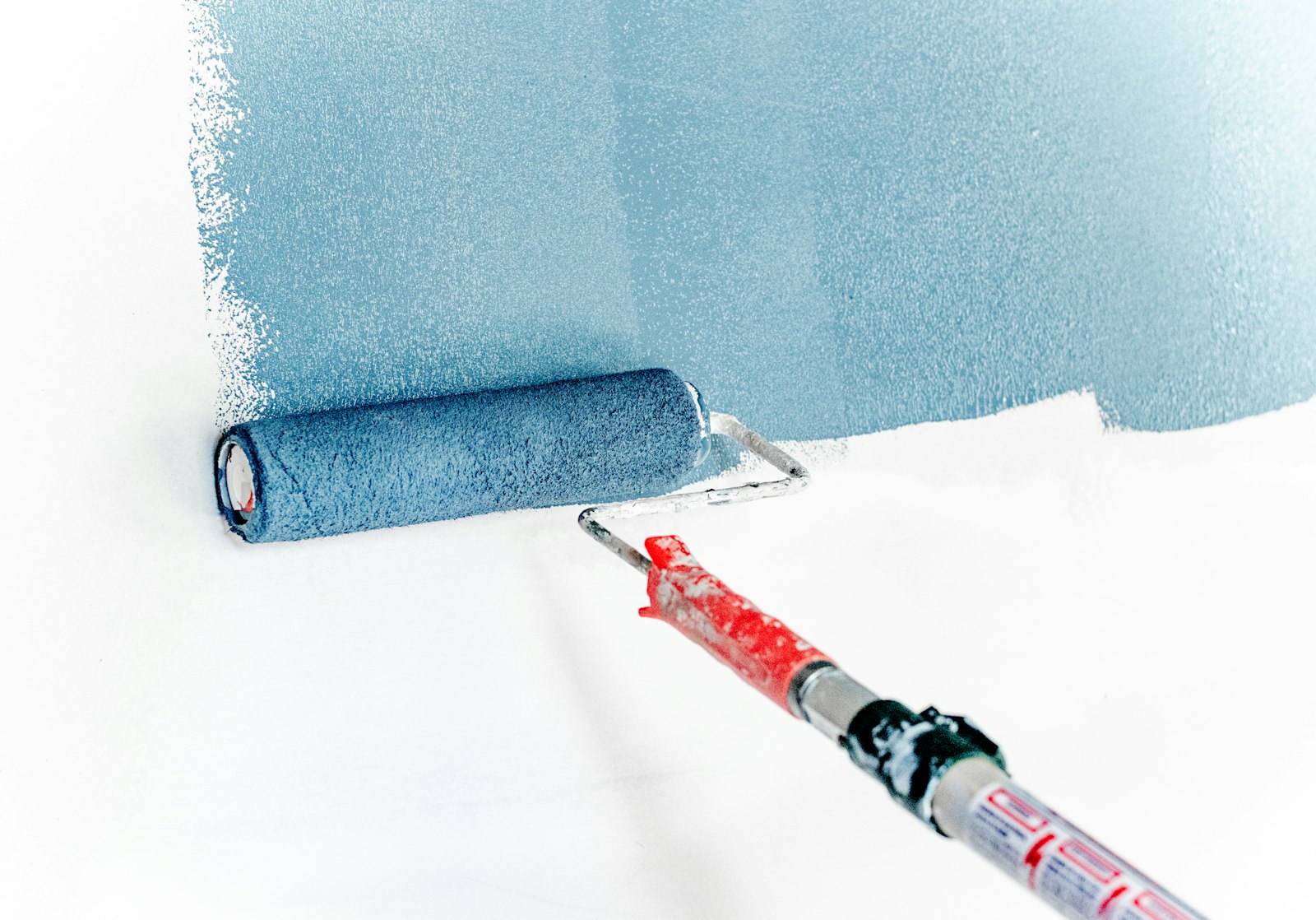 A paint roller applying blue-grey paint to a white wall.